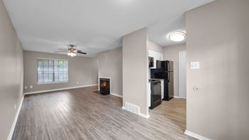 A spacious living room with a fireplace and a kitchenette in the background.